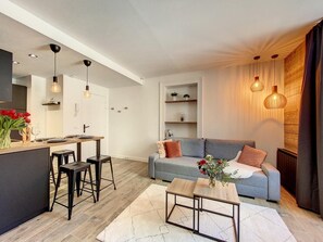 Een moderne woonkamer met een grijze bank, een salontafel en een keukenhoek met een eettafel en barkrukken.
