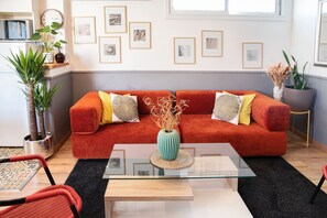 A modern living room with a red sofa, a glass coffee table, and a variety of framed pictures on the wall. - Family House 10 pers, parking – métro line 7 (Villejuif)