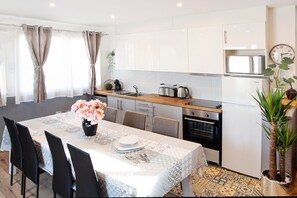 A modern kitchen with white cabinets, a wooden countertop, and a dining area with a lace tablecloth. - Family House 10 pers, parking – métro line 7 (Villejuif)