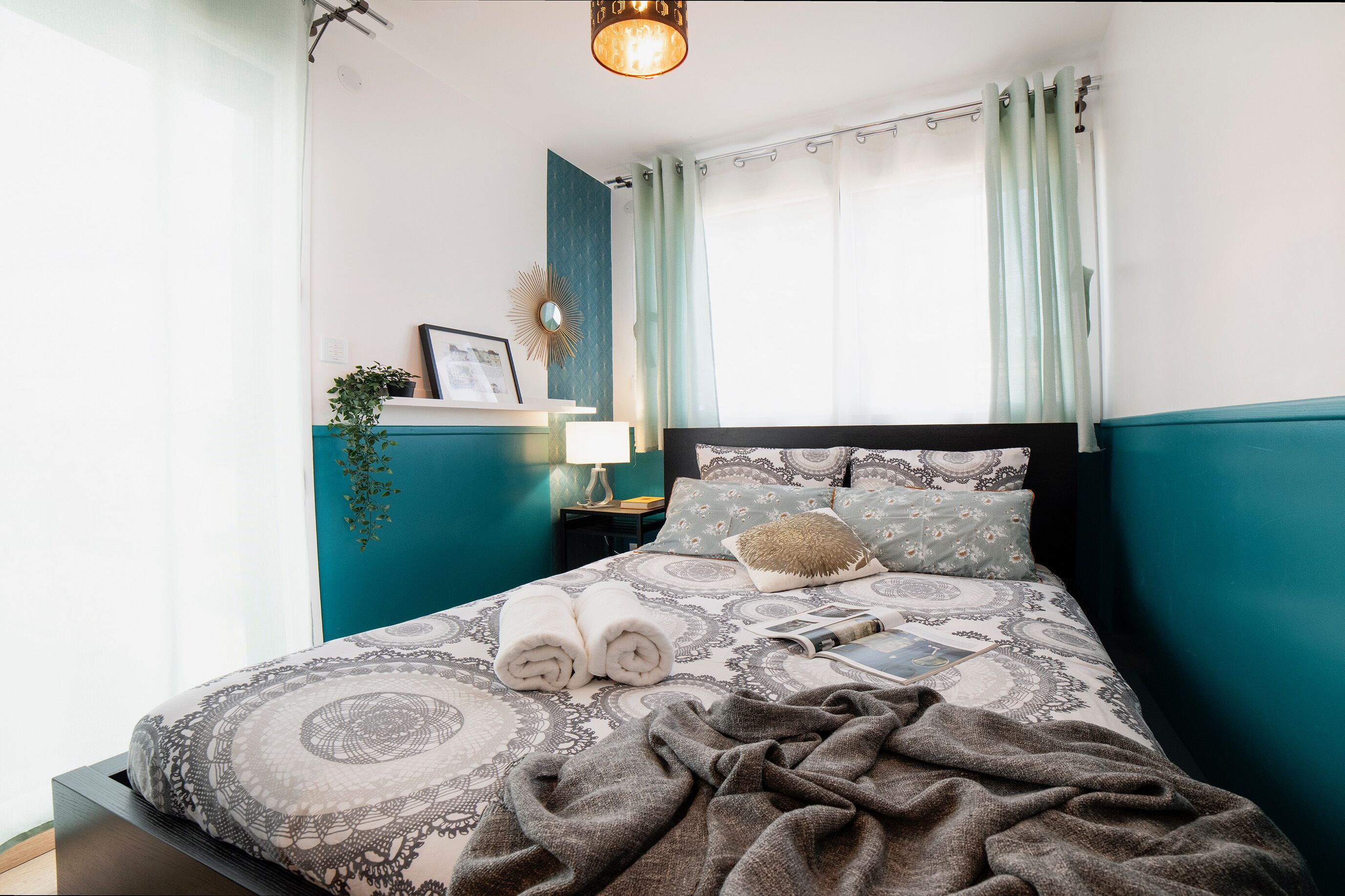 Un lit bien fait, avec une literie à motifs, une lampe de chevet et une petite plante posée sur une étagère.