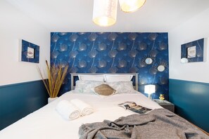 A neatly made bed with a blue patterned headboard, a bedside lamp, and a framed picture on the wall. - Family House 10 pers, parking – métro line 7 (Villejuif)