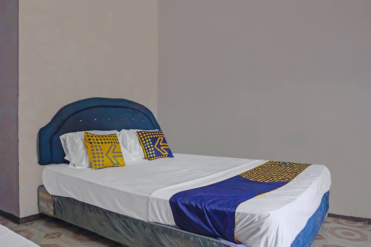 A neatly made bed with a blue headboard, white bedding, and decorative pillows with geometric patterns.