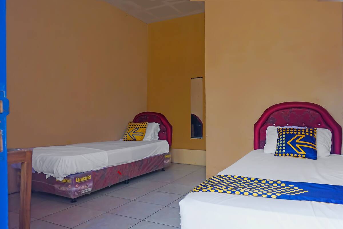 A room with two beds, one with a red headboard and one with a white headboard, both with patterned bedspreads.