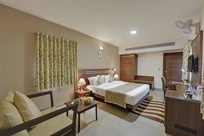 A hotel room with a bed, bedside table, lamp, and a desk with a chair. - The Maharana Bagh (Udaipur)