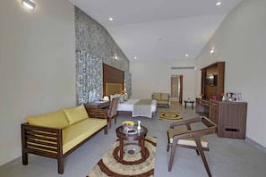 A modern hotel room with a sofa, armchair, and a dining table with a vase and fruit bowl. - The Maharana Bagh (Udaipur)
