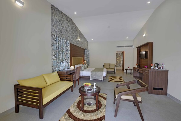 A modern hotel room with a sofa, armchair, and a dining table with a vase and fruit bowl.