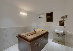 Un baño con pared de mármol, tocador de madera, toallero y lavamanos empotrado.