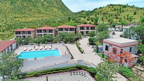 Un hotel con piscina, varias edificaciones y montañas al fondo.