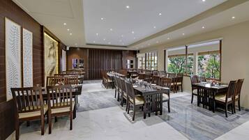 Un comedor amplio con varias mesas y sillas, suelo de mármol y ventanas grandes con vistas a zonas verdes.