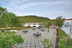 Un patio con mesas al aire libre, un edificio al fondo y un paisaje montañoso.