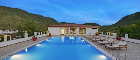 A swimming pool with lounge chairs and a building with a red roof in the background.