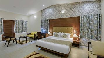 Habitación de hotel con una cama grande, dos mesitas de noche con lámparas, un sofá, una silla y una pequeña mesa.