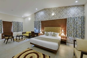 A hotel room with a large bed, two bedside tables with lamps, a sofa, a chair, and a small table. - The Maharana Bagh (Udaipur)