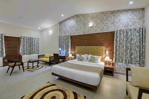 Habitación de hotel con una cama grande, dos mesitas de noche con lámparas, un sofá, una silla y una pequeña mesa.