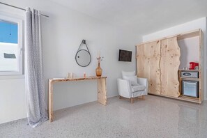 Een kamer met een houten bureau, een witte stoel, een klein kastje en een tv aan de muur.