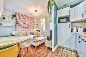 Una cocina moderna con armarios blancos, un microondas y un tostador. Hay una zona de comedor con una mesa y sillas de madera.
