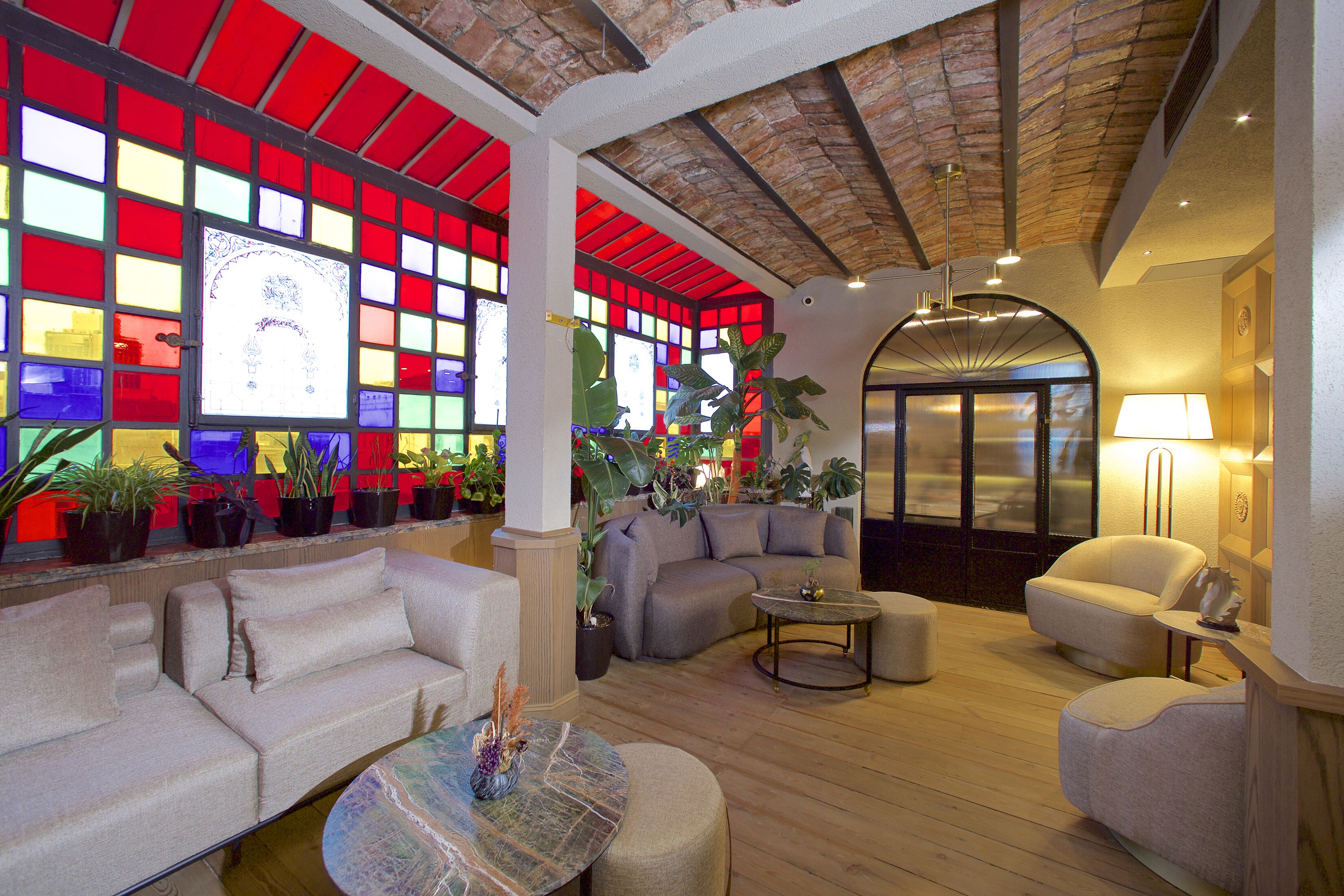 A spacious lobby with a high ceiling, a seating area with sofas and a coffee table, and a large window with colorful stained glass.