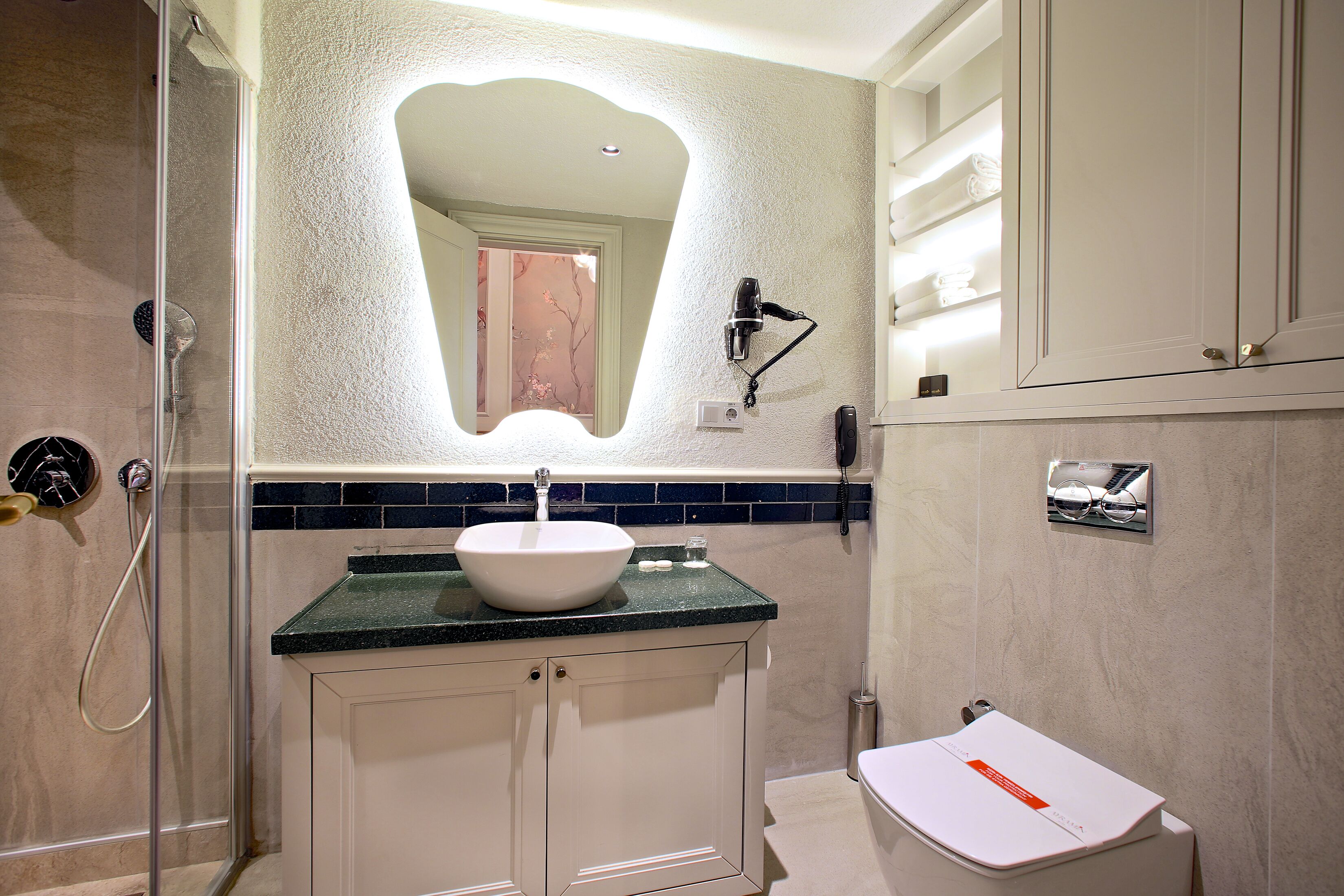 A bathroom with a glass shower enclosure, a white sink with a green countertop, and a white toilet.