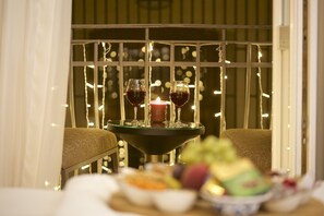 Une table avec deux verres de vin rouge, une bougie allumée et un saladier de fruits.