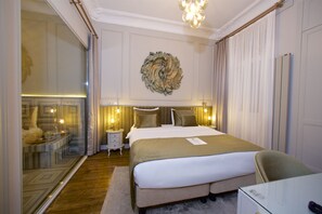 Une chambre d’hôtel avec un grand lit, une table de chevet avec une lampe, un miroir et une vue sur la ville par une grande fenêtre.
