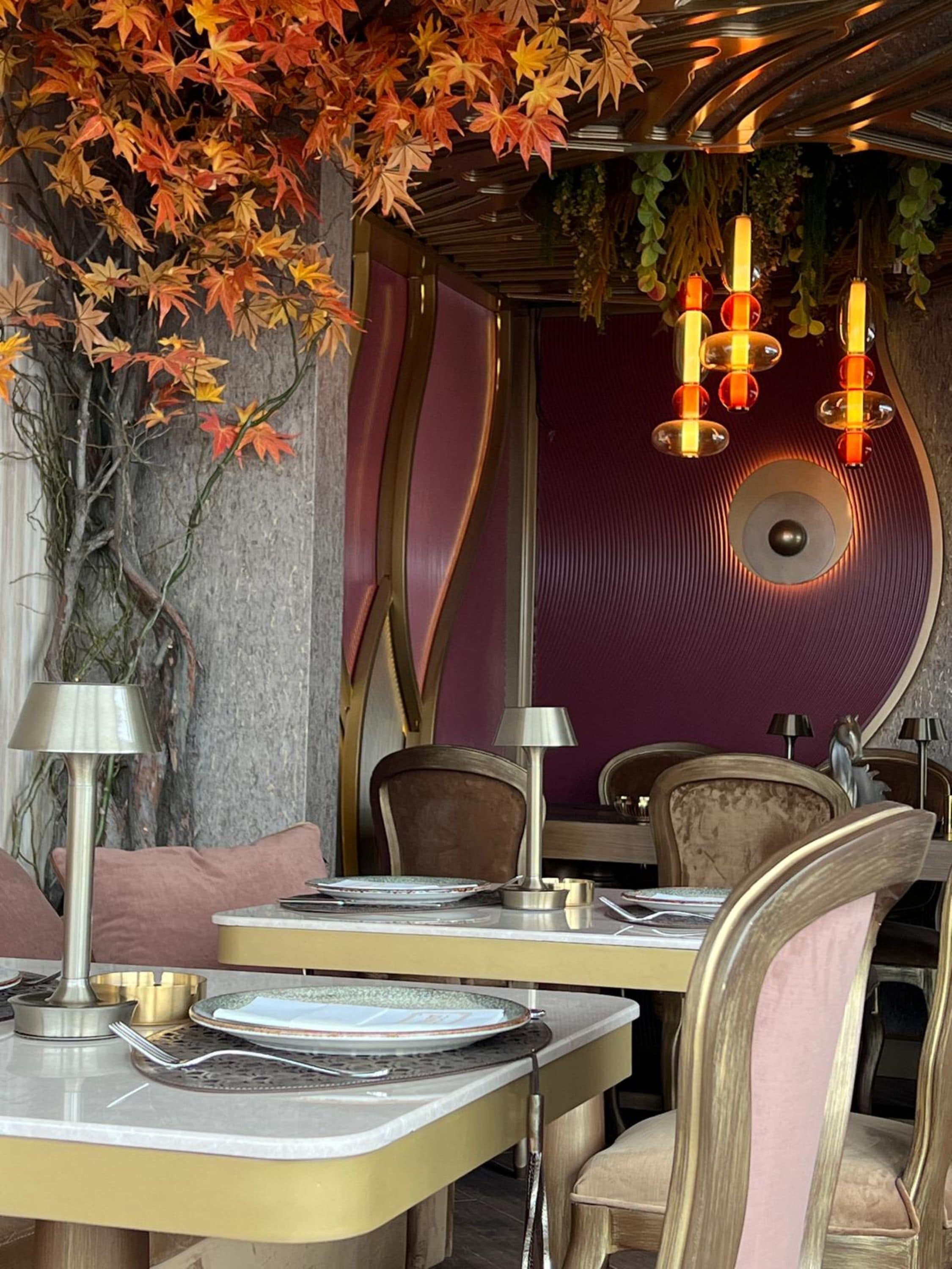 A dining area with tables set for two, chairs, and a decorative wall with autumn leaves.