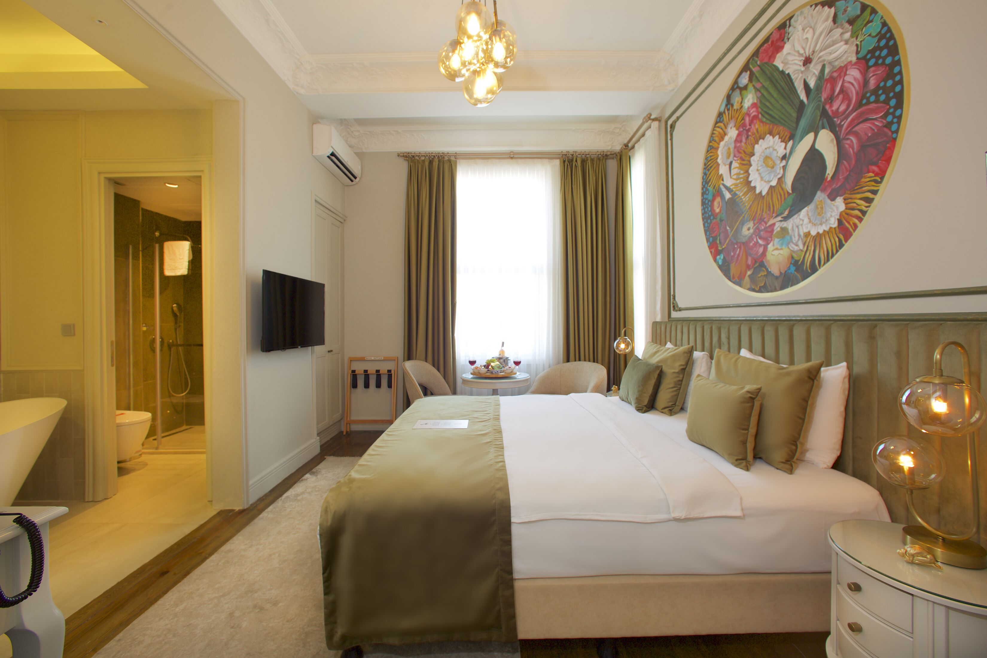 A hotel room with a large bed, a bedside table with a lamp, a flat-screen TV, and a painting on the wall.