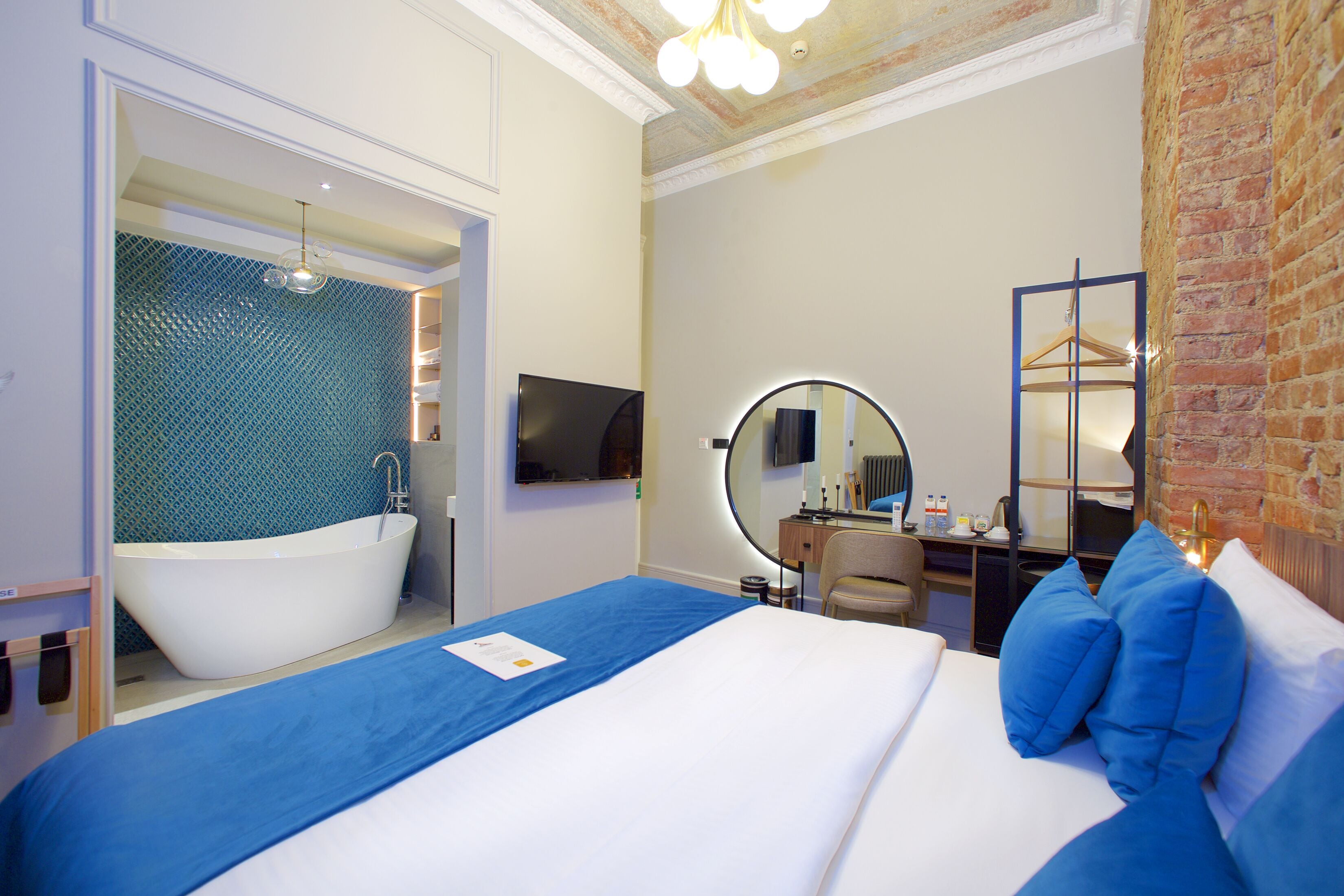 A hotel room with a large bed, a bathtub, a desk with a chair, a TV, and a mirror.
