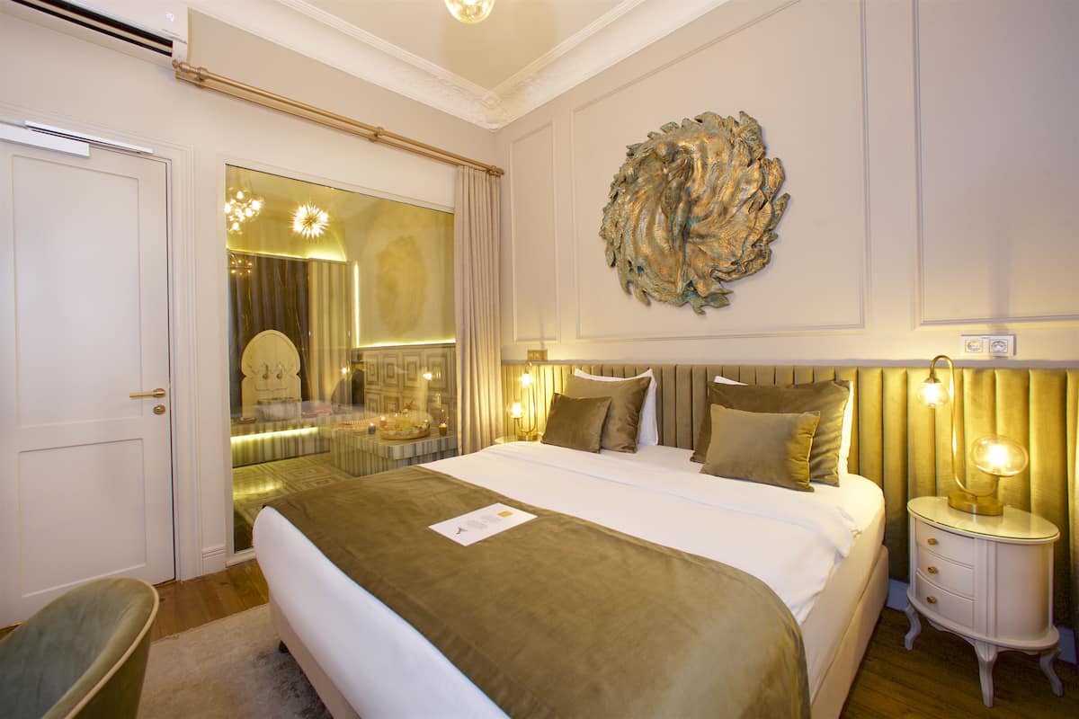 A hotel room with a large bed, a bedside table with a lamp, a mirror, and a decorative wall piece.