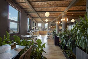 Un restaurante amplio con pisos de madera, ventanas grandes y abundantes plantas.