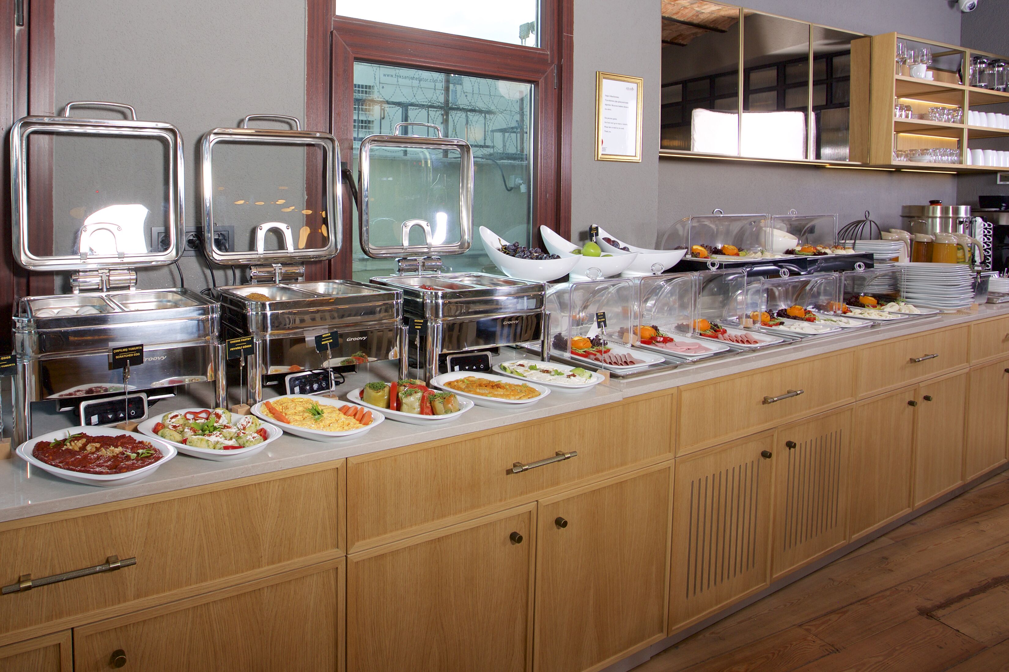 Buffet com diversos pontos de comida e janela com vista para prédios.