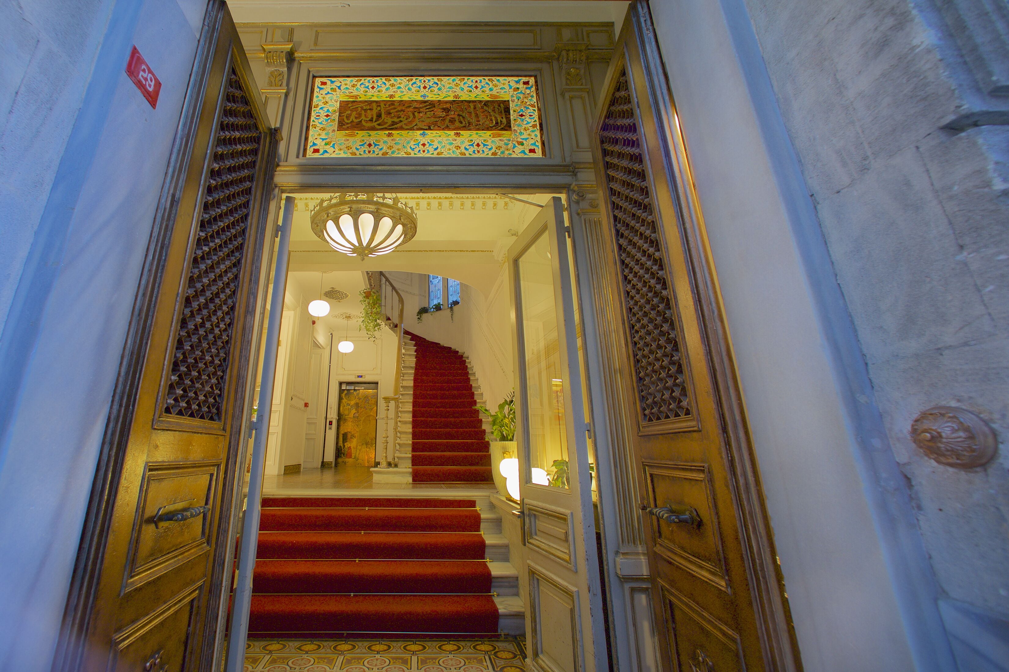 A grand staircase with red carpeted steps leading to a door with intricate designs.