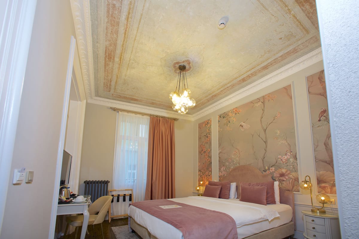 A bedroom with a bed, a desk, a chair, a radiator, and a window with curtains.