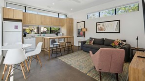 A modern kitchen with wooden cabinets, a white refrigerator, and a dining area with white chairs. - Modern 1-bedroom Apartment - 80 Walkscore! (Phoenix)