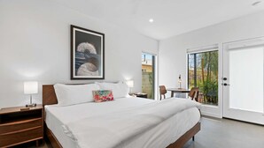 Une chambre d’hôtel moderne dotée d’un grand lit, d’une table de chevet, d’un bureau avec une chaise et d’une porte-fenêtre coulissante donnant sur un balcon.