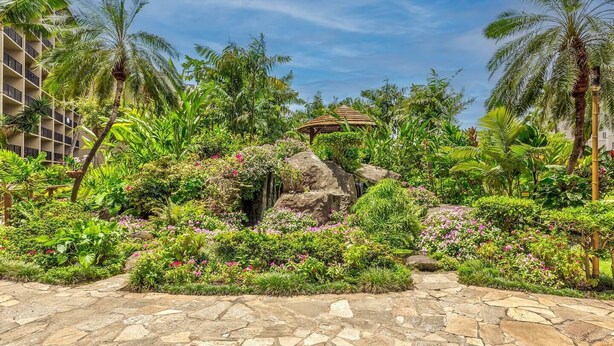 A lush garden with a waterfall, palm trees, and a stone pathway.