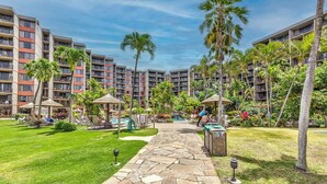A hotel courtyard with a stone pathway, lounge chairs, palm trees, and a pool area.