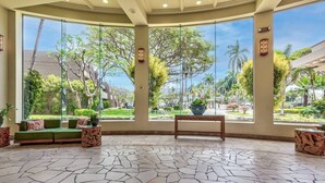 A spacious lobby with a green sofa, a wooden bench, and a large window offering a view of a landscaped garden.