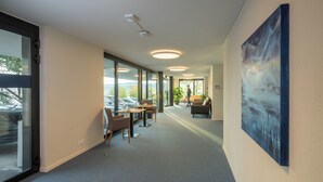 Un intérieur moderne avec un long couloir, de grandes fenêtres et un tableau accroché au mur.