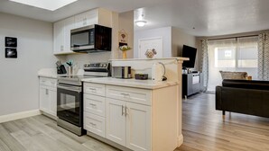 A modern kitchen with white cabinetry, a built-in microwave, and a stove. There is a dining area with a black sofa and a TV. - Dreamy Vegas Strip area condo (Las Vegas)