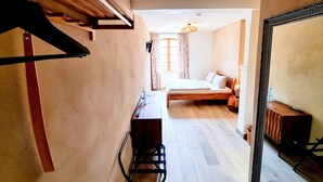Ein Schlafzimmer mit einem hölzernen Bett, einem Schreibtisch und einem Stuhl. An der Wand befindet sich ein Spiegel und ein Fenster mit Vorhängen.