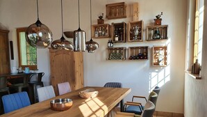 Ein Essbereich mit Holztisch, Stühlen, hängenden Pendelleuchten und Wandregalen mit Flaschen und einer Trophäe.