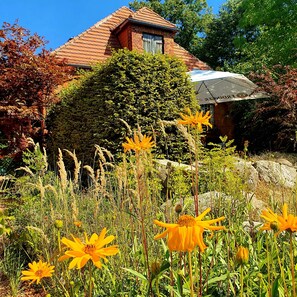 A house with a red-tiled roof, surrounded by lush greenery and flowering plants.
