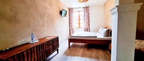 A bedroom with a wooden bed, a bedside table, a television, and a window with curtains.