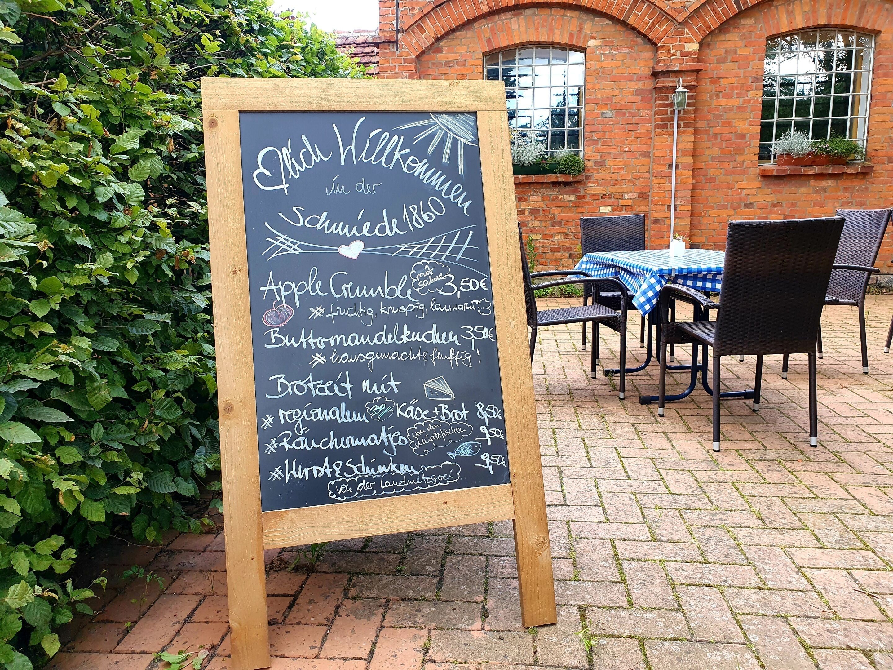 A chalkboard menu outside a brick building with a table and chairs nearby.