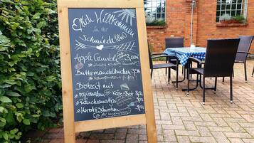 A chalkboard menu outside a brick building with a table and chairs nearby.