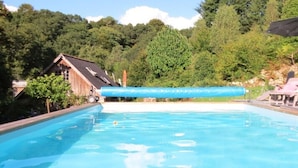 Una piscina con lettini e un ombrellone, immersa nel verde e con un edificio in legno.