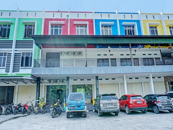 A multi-story building with colorful facades, a parking area with several cars and motorcycles, and a gated entrance. - OYO 92152 Hotel The Wong (Baturaja)
