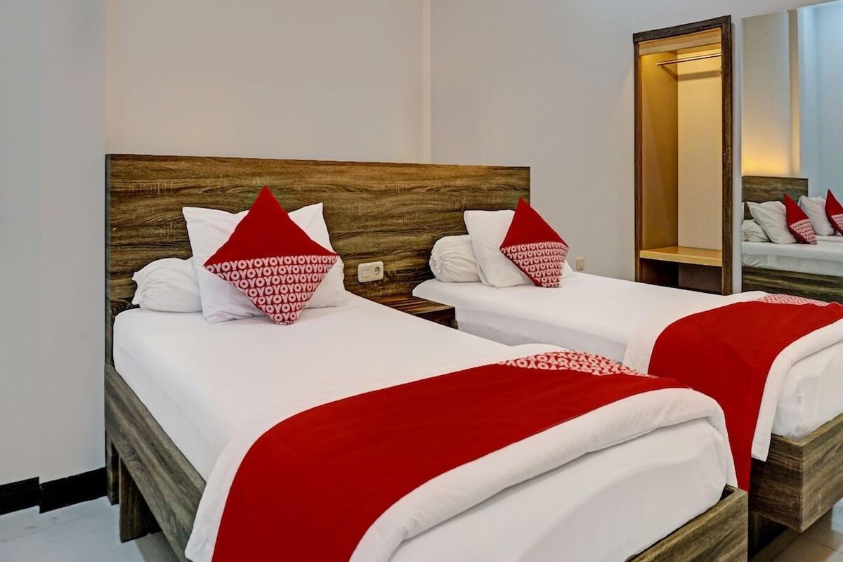 Habitación de hotel con dos camas, cada una con ropa de cama blanca y detalles rojos, cabeceros de madera y un espejo grande en la pared.
