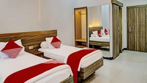 Une chambre d’hôtel avec deux lits, chacun doté de draps blancs et d’oreillers rouges, d’une tête de lit en bois, d’un miroir et d’une armoire.