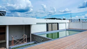Une piscine sur le toit, avec une terrasse carrelée et un bâtiment moderne en arrière-plan.